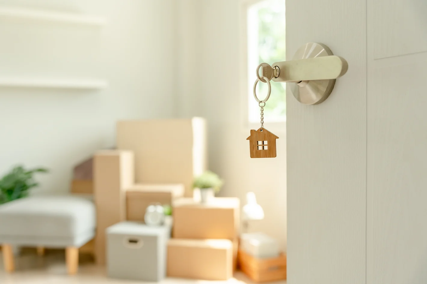 Huissleutel in een deur met verhuisdozen in een lichte woning.
